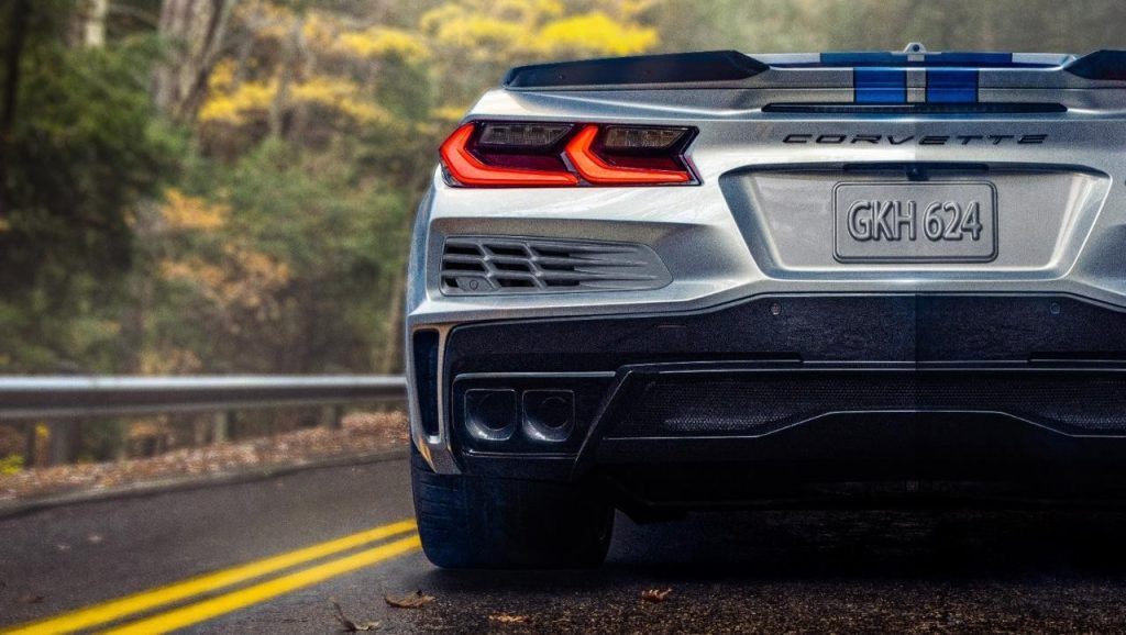Close-up rear-view of 2024 Chevrolet Corvette E-Ray 3LZ convertible in Silver Flare with Electric Blue stripe package parked on a road in front of trees. Pre-production model shown. Actual production model may vary. Model year 2024 Corvette E-Ray available 2023.