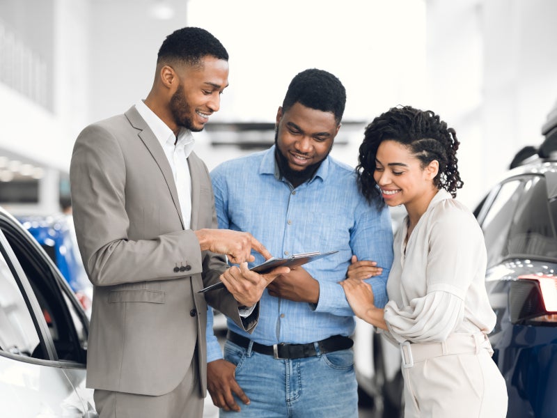 Salesman reviewing paperwork with couple in car dealership