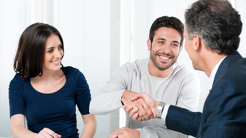 couple smiling talking to salesman, men shaking hands